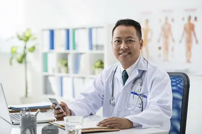Smiling general practitioner with smartphone in his hand looking at camera