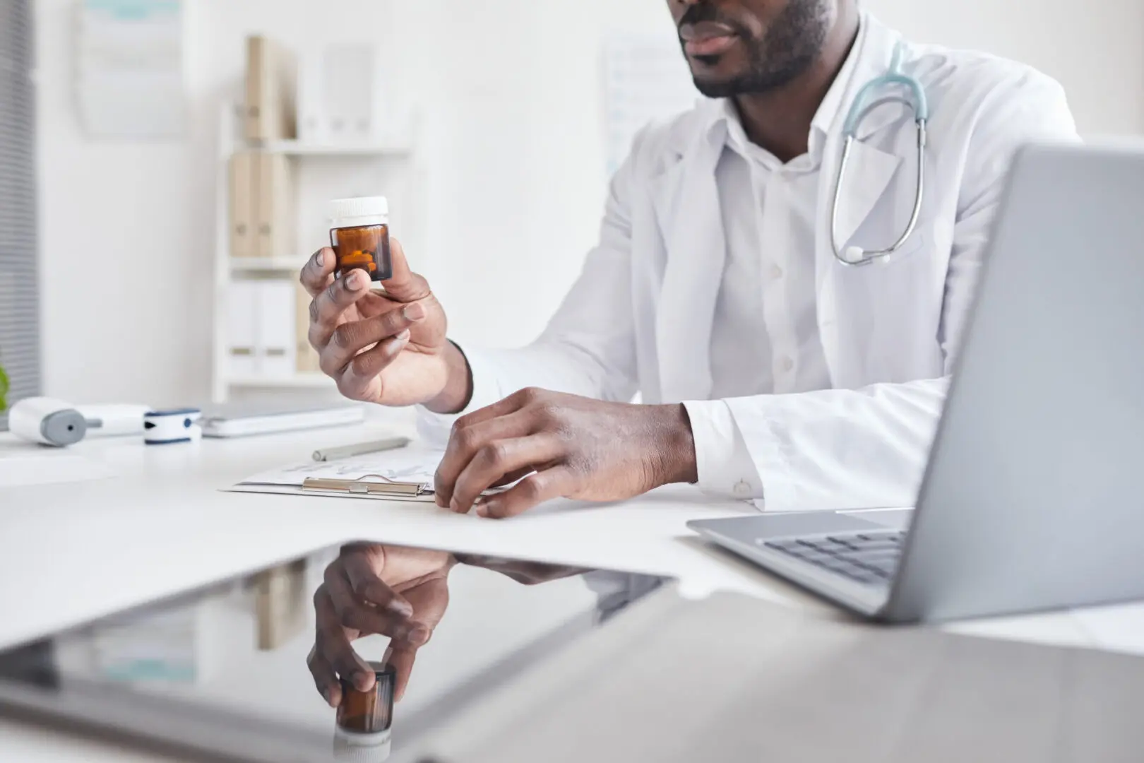A doctor is holding a pill bottle while sitting at his desk.